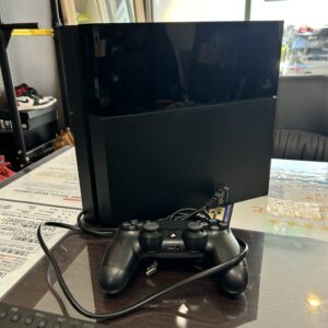 高松市のトレリバで買取したPS4（PlayStation 4）。テーブルの上に置かれた黒い本体と純正コントローラー、電源ケーブルの画像。