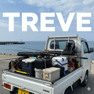 **海辺の埠頭に停まった軽トラックの荷台に、釣り竿、クーラーボックス、バッカン、長靴など、大量の釣具が積み込まれている様子。**背景には青い海と空、そして防波堤が見える。