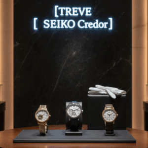 「【TREVE SEIKO Credor】」のブルーネオンロゴが黒大理石の壁面に映える、高級感溢れる査定ラウンジ。中央の円形ウッドテーブルには、ゴールドブレスのドレスウォッチ、レザーストラップのコンプリケーションモデルなど、セイコーとクレドールの至高のタイムピース3本が並んでいる。傍らには白い接客用手袋が添えられ、高松市の時計買取専門店「TREVE」による、国産時計の精密な機構と外装美を敬意を持って鑑定するイメージ。