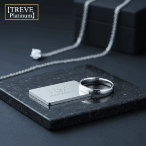 「【TREVE Platinum】」のロゴが左上に配置された、シックな黒背景の査定デスク。手前の黒御影石のプレート上には、「PT900 999.5 FINE PLATINUM」と刻印されたプラチナプレートと、滑らかな光沢のプラチナリングが置かれている。奥には一粒ダイヤモンドのプラチナネックレスが美しくレイアウトされ、高松市のプラチナ買取専門店「TREVE」による精密な鑑定をイメージしている。