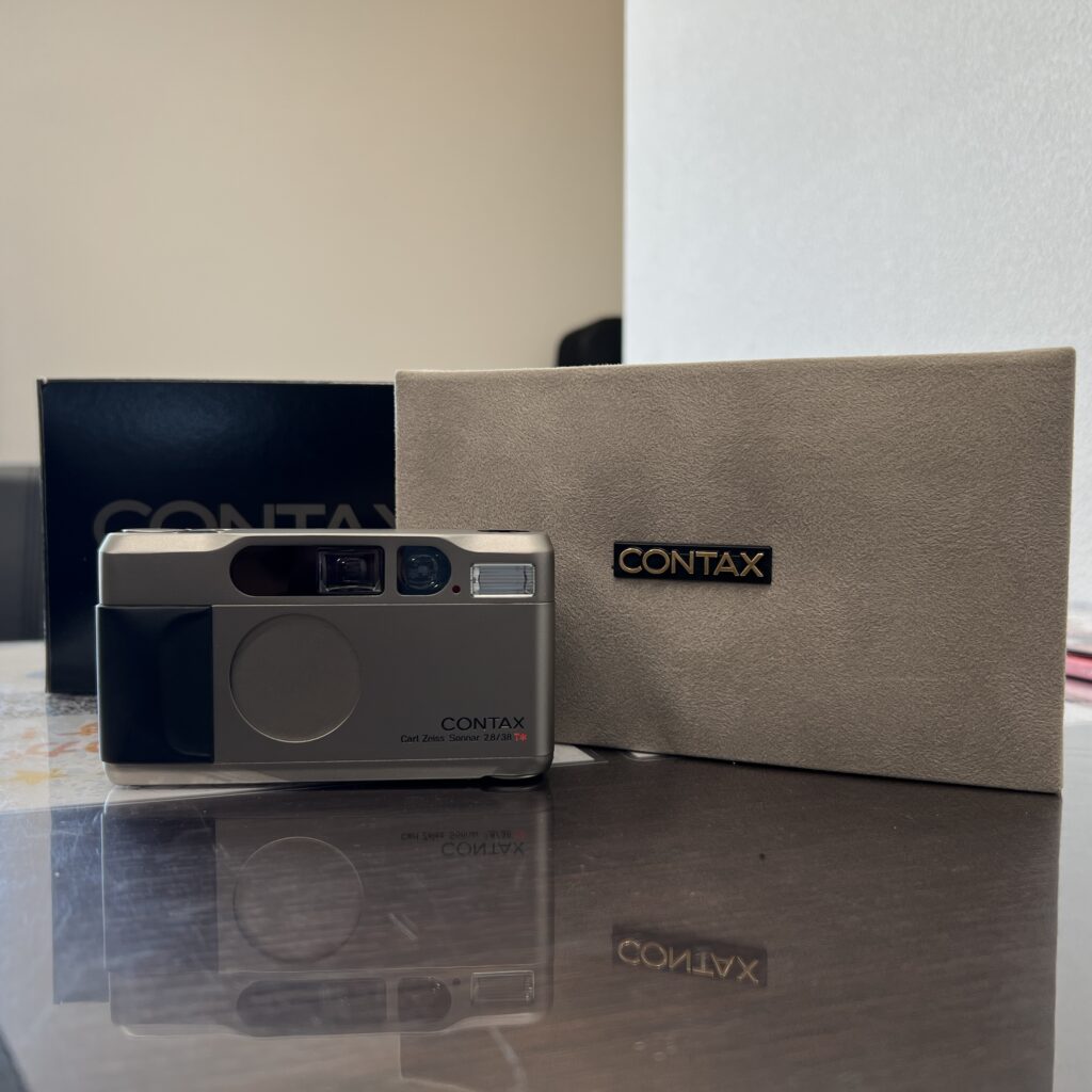 高松市のトレリバで買取したCONTAX T2 フィルムカメラと高級感のある純正ケース・ストラップの画像。