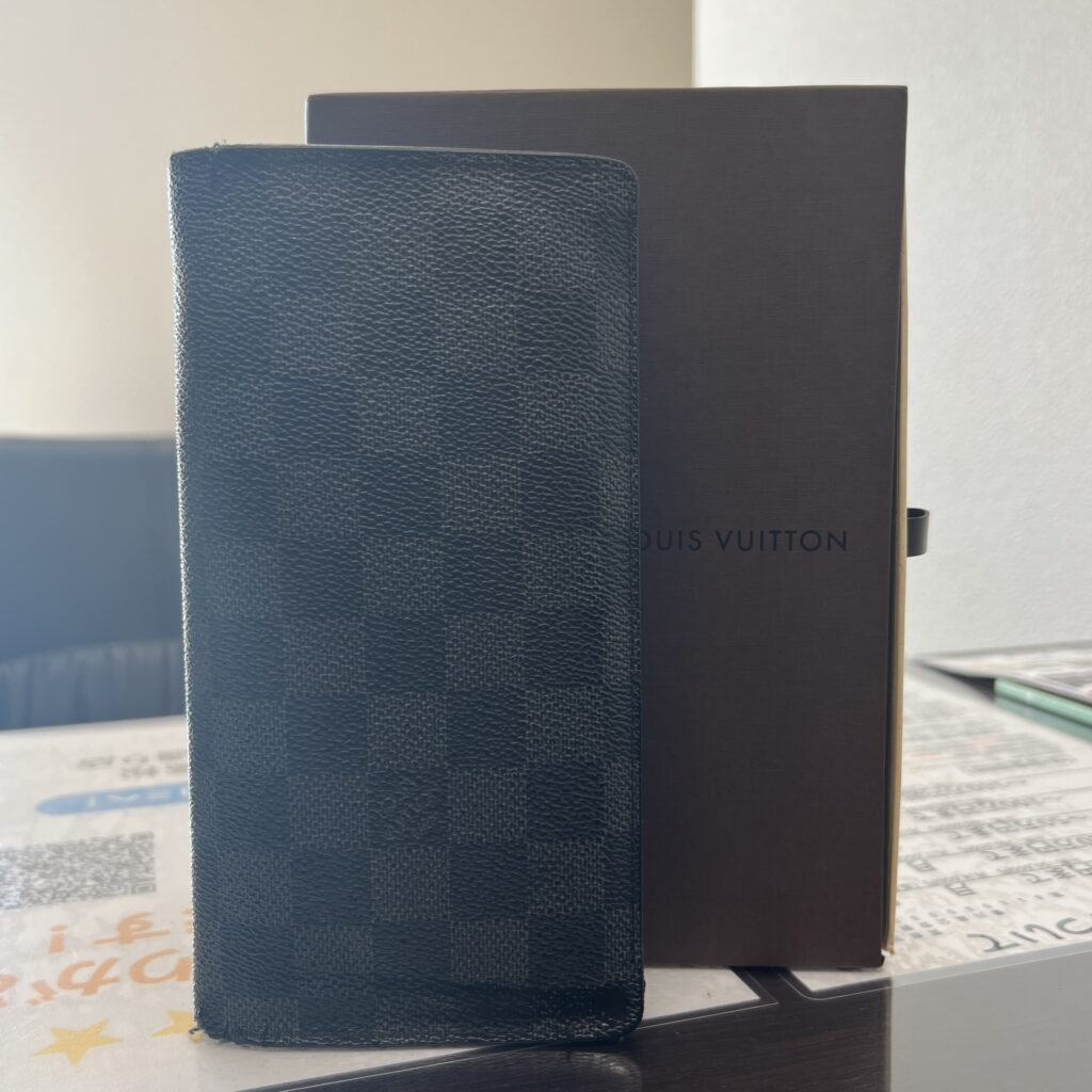 高松市のトレリバで買取したルイヴィトンのメンズ長財布「ポルトフォイユ・ブラザ（ダミエ・グラフィット）」。茶色の箱の前に立てかけられた画像。