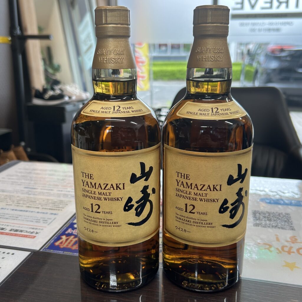 高松市のトレリバで買取したサントリーウイスキー山崎12年。テーブルの上に置かれた、未開封の2本のウイスキーボトルの画像。
