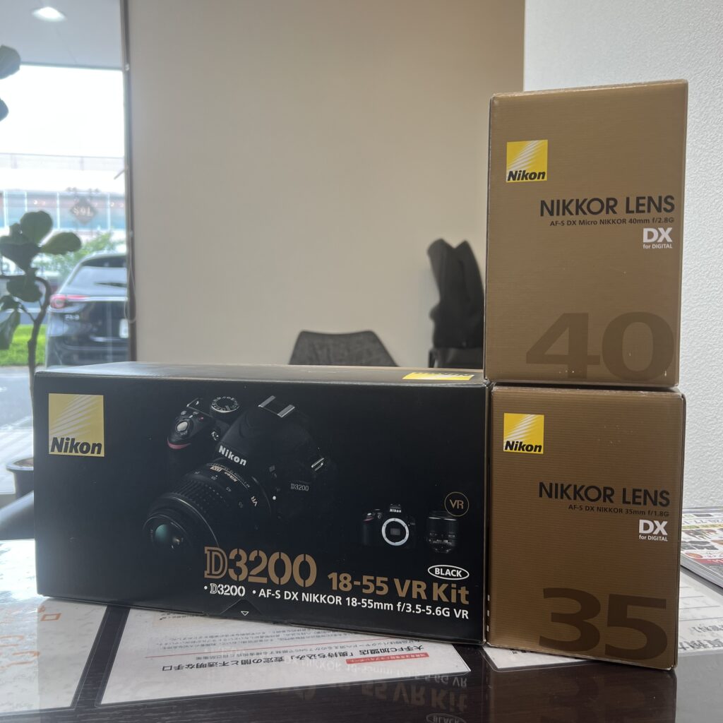 高松市のトレリバで買取したニコン（Nikon）のデジタル一眼レフカメラ「D3200」と交換レンズ各種。テーブルの上に並べられた、黒いキット箱と茶色いレンズ化粧箱の画像。