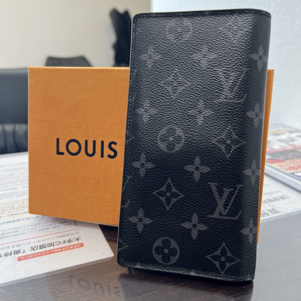 高松市のトレリバで買取したルイ・ヴィトン（LOUIS VUITTON）の長財布「ポルトフォイユ・ブラザ」。テーブルの上に立てて置かれたモノグラムエクリプスの本体と、後ろにあるオレンジの純正箱の画像。