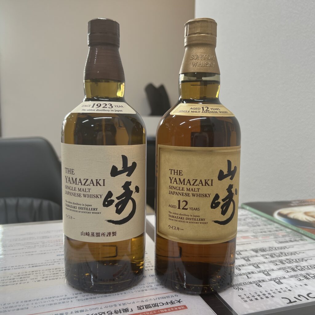 高松市のトレリバで買取したサントリーウイスキー山崎12年とNV。テーブルの上に並べられた未開封のシングルモルトウイスキーボトルの画像。