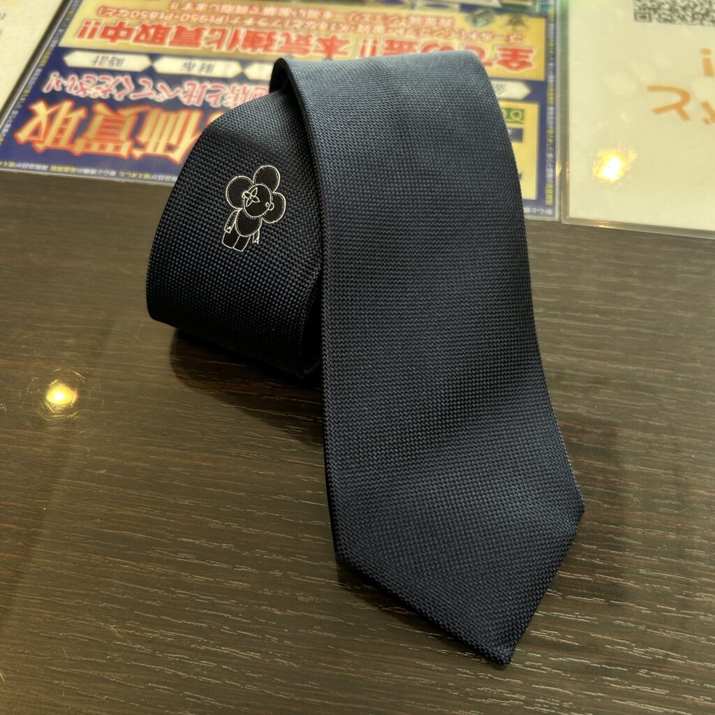 高松市のトレリバで買取したルイ・ヴィトン（LOUIS VUITTON）のシルクネクタイ。テーブルの上に置かれたネイビーの本体とヴィヴィエンヌ刺繍の画像。